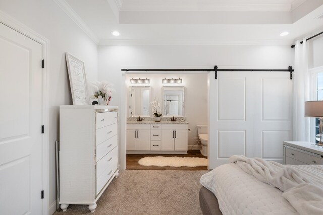 bedroom featuring connected bathroom, crown molding, light colored carpet, and a barn door