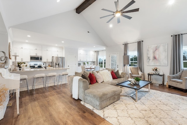 living room featuring high vaulted ceiling, sink, ceiling fan, beamed ceiling, and wood-type flooring