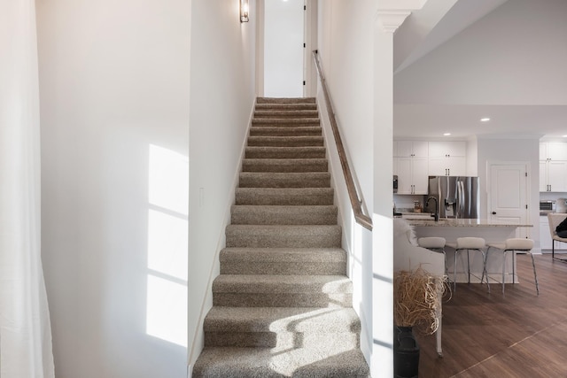 staircase featuring ornate columns, wood-type flooring, a wealth of natural light, and a towering ceiling