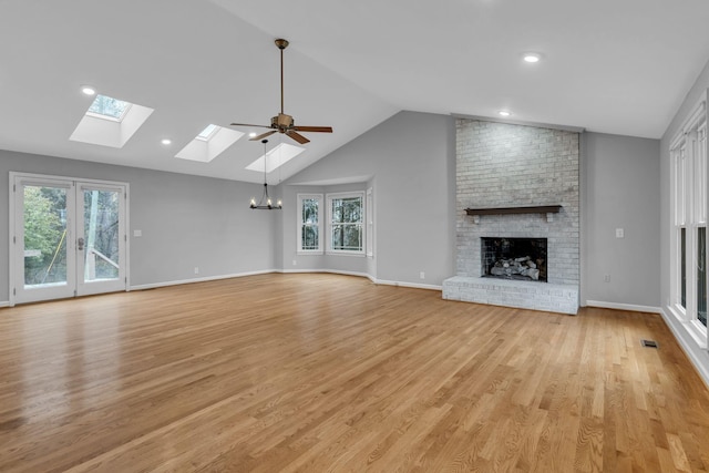 unfurnished living room featuring vaulted ceiling with skylight, plenty of natural light, a brick fireplace, and light hardwood / wood-style flooring