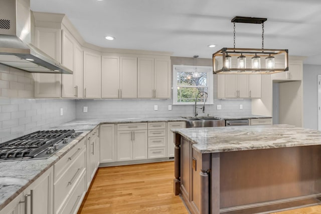 kitchen featuring wall chimney exhaust hood, decorative light fixtures, light hardwood / wood-style floors, white cabinetry, and stainless steel gas cooktop