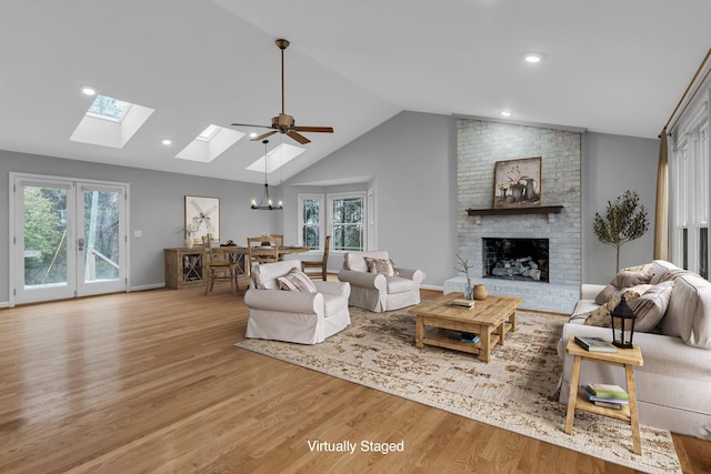 living room with vaulted ceiling with skylight, plenty of natural light, ceiling fan with notable chandelier, and light hardwood / wood-style flooring