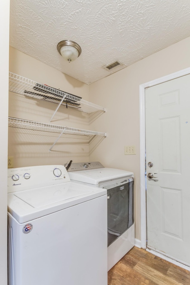 laundry area with washing machine and dryer, light wood-type flooring, and a textured ceiling