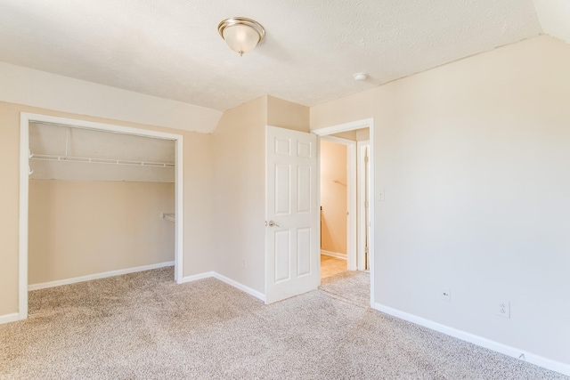 unfurnished bedroom featuring a textured ceiling, lofted ceiling, light carpet, and a closet