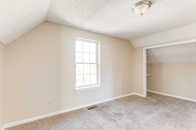 unfurnished bedroom with a textured ceiling, lofted ceiling, carpet floors, and a closet