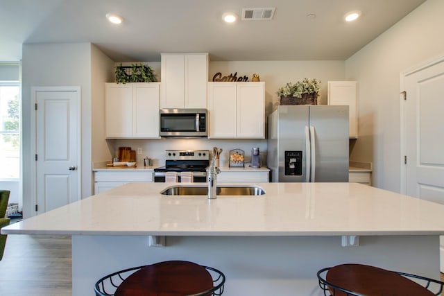 kitchen featuring white cabinetry, sink, light stone counters, an island with sink, and appliances with stainless steel finishes