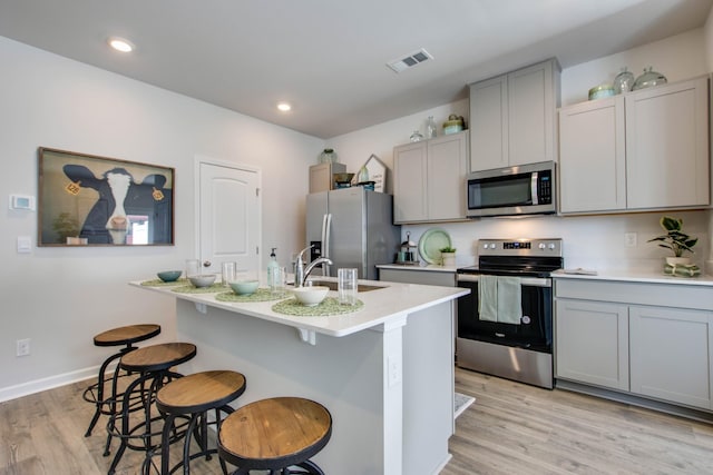 kitchen with sink, stainless steel appliances, gray cabinets, a breakfast bar, and light wood-type flooring