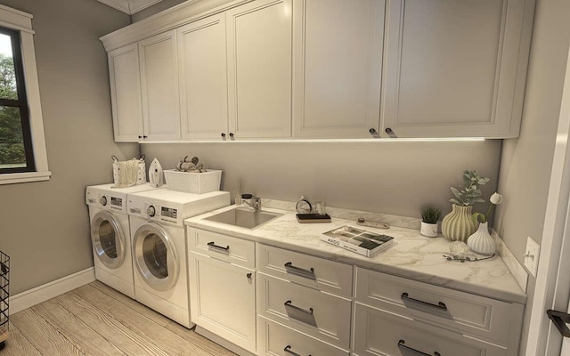 clothes washing area featuring washer and clothes dryer, cabinets, light wood-type flooring, and sink