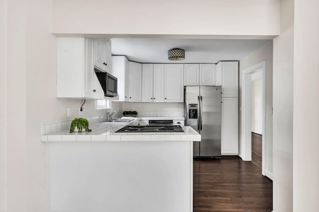 kitchen featuring appliances with stainless steel finishes, kitchen peninsula, dark wood-type flooring, tile countertops, and white cabinets