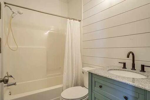 full bathroom with shower / bath combination with curtain, vanity, toilet, and wood walls