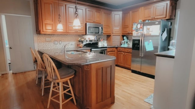 kitchen featuring sink, stainless steel appliances, kitchen peninsula, light hardwood / wood-style floors, and pendant lighting