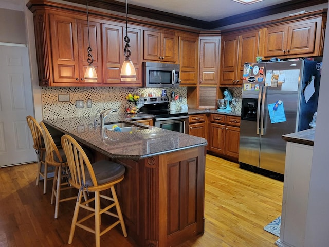 kitchen featuring sink, stainless steel appliances, kitchen peninsula, decorative light fixtures, and a kitchen bar