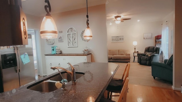 kitchen featuring a kitchen breakfast bar, dark stone counters, sink, decorative light fixtures, and light hardwood / wood-style floors