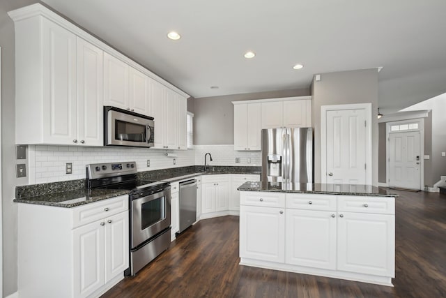 kitchen with backsplash, white cabinetry, stainless steel appliances, and dark stone counters