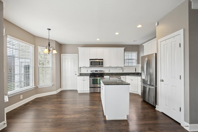 kitchen featuring hanging light fixtures, stainless steel appliances, a kitchen island, a notable chandelier, and white cabinets