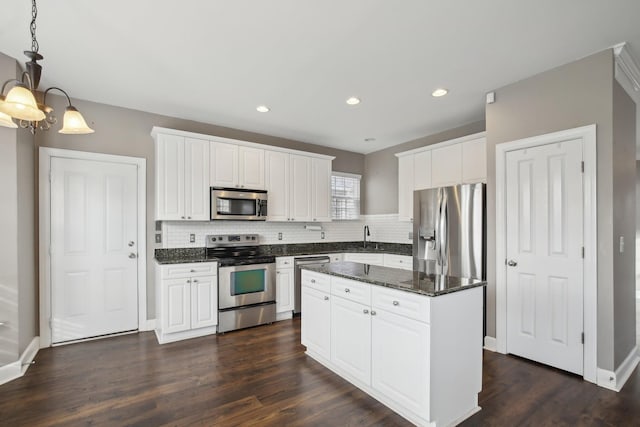 kitchen with appliances with stainless steel finishes, pendant lighting, white cabinets, dark hardwood / wood-style floors, and a kitchen island