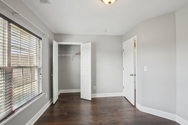 unfurnished bedroom featuring multiple windows, a closet, and dark hardwood / wood-style floors