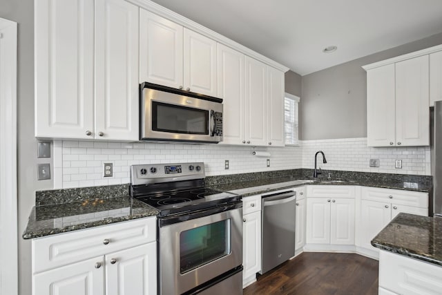 kitchen with stainless steel appliances, sink, dark stone countertops, white cabinets, and dark hardwood / wood-style floors