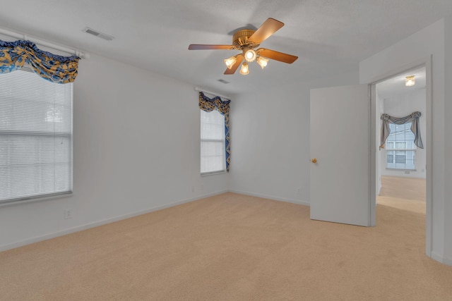 empty room with light carpet, ceiling fan, and a healthy amount of sunlight