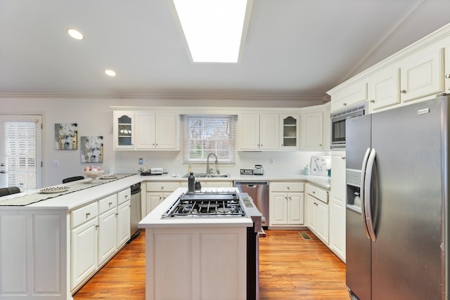 kitchen featuring white cabinetry, appliances with stainless steel finishes, light wood-type flooring, a kitchen island, and ornamental molding