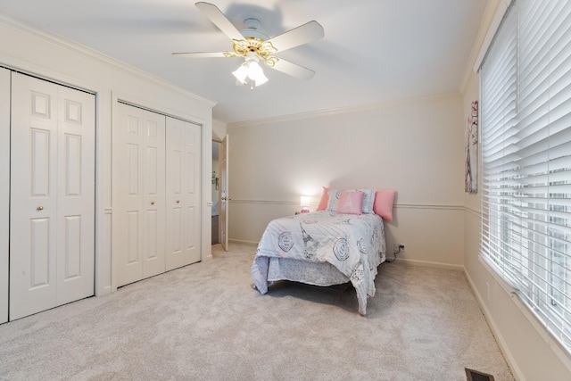 bedroom with light carpet, multiple closets, ceiling fan, and ornamental molding