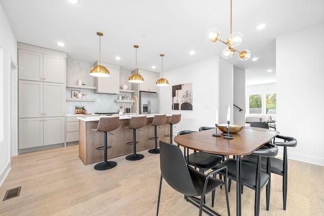 dining space with light hardwood / wood-style floors, a notable chandelier, and sink