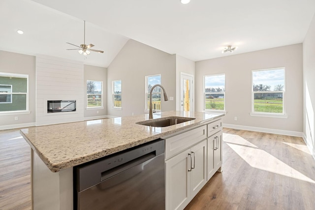 kitchen featuring light stone countertops, white cabinetry, sink, stainless steel dishwasher, and a center island with sink