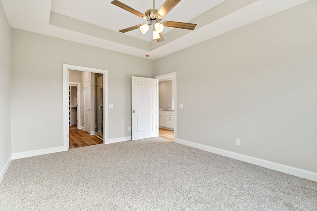 unfurnished bedroom with a raised ceiling, ceiling fan, and light carpet