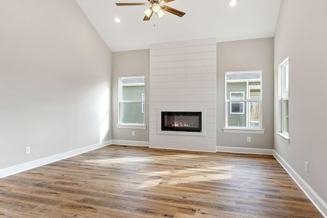 unfurnished living room with hardwood / wood-style floors, ceiling fan, a fireplace, and high vaulted ceiling