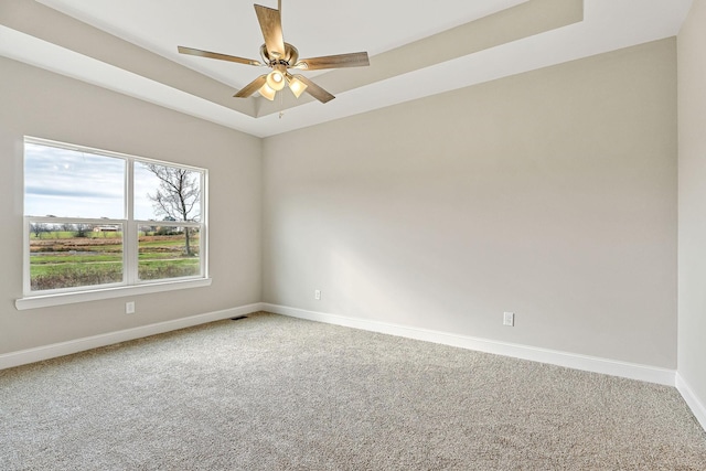 carpeted empty room with ceiling fan and a raised ceiling