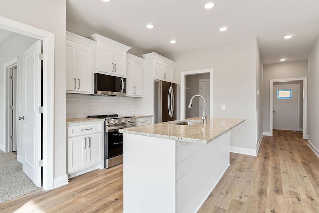 kitchen with appliances with stainless steel finishes, sink, light hardwood / wood-style flooring, white cabinets, and an island with sink