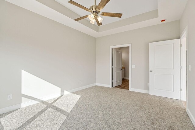 unfurnished bedroom with carpet floors, a tray ceiling, and ceiling fan