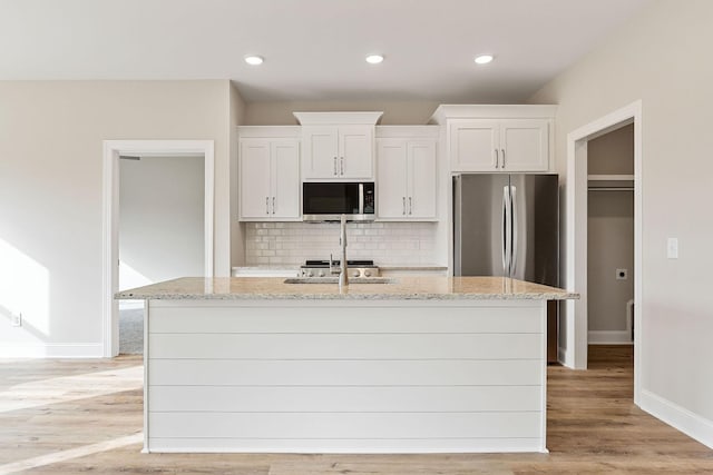 kitchen featuring a kitchen island with sink, white cabinets, light wood-type flooring, appliances with stainless steel finishes, and light stone counters