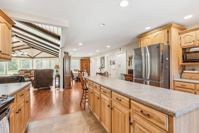 kitchen featuring light brown cabinetry, stainless steel refrigerator, light hardwood / wood-style flooring, and lofted ceiling with beams