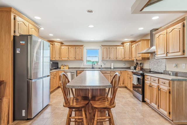 kitchen featuring wall chimney exhaust hood, stainless steel appliances, a kitchen bar, light brown cabinetry, and a kitchen island