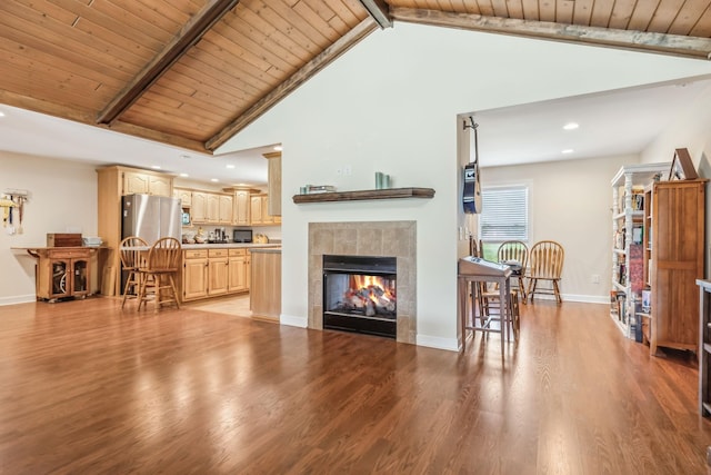 living room with beam ceiling, a tiled fireplace, light hardwood / wood-style flooring, and wood ceiling