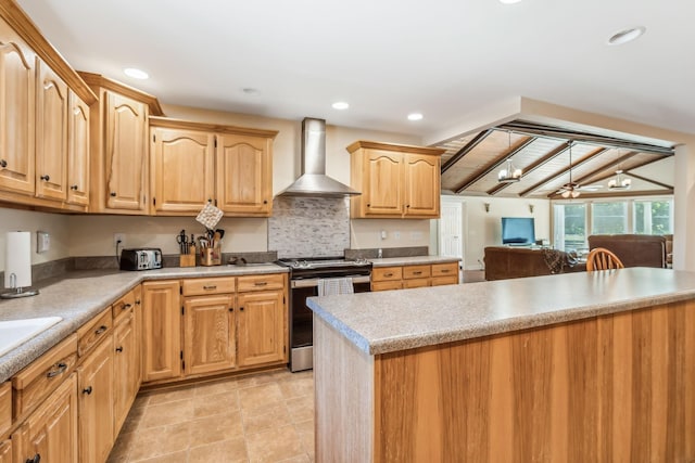 kitchen featuring ceiling fan, wall chimney range hood, tasteful backsplash, stainless steel range oven, and light brown cabinetry