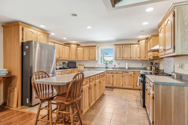 kitchen featuring light brown cabinetry, a breakfast bar, stainless steel appliances, sink, and a kitchen island