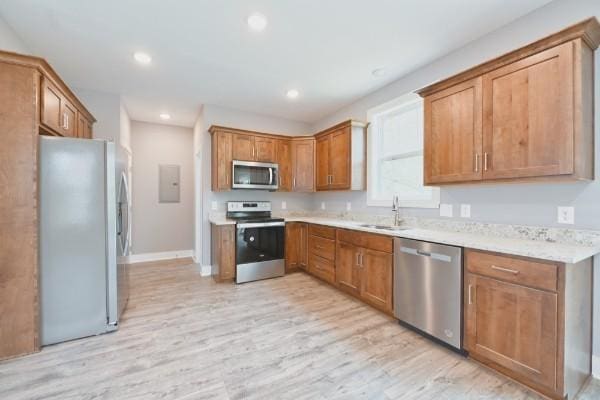 kitchen with electric panel, sink, light hardwood / wood-style floors, light stone counters, and stainless steel appliances