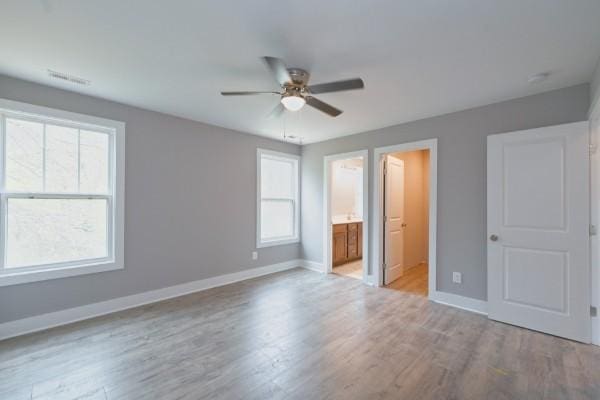 unfurnished bedroom featuring ensuite bathroom, ceiling fan, and multiple windows