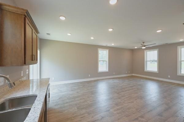 kitchen featuring ceiling fan, light stone countertops, light wood-type flooring, and sink