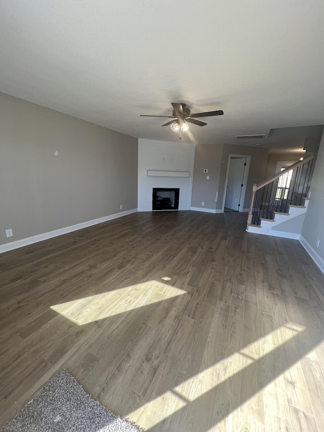 unfurnished living room with ceiling fan, a large fireplace, and dark hardwood / wood-style flooring