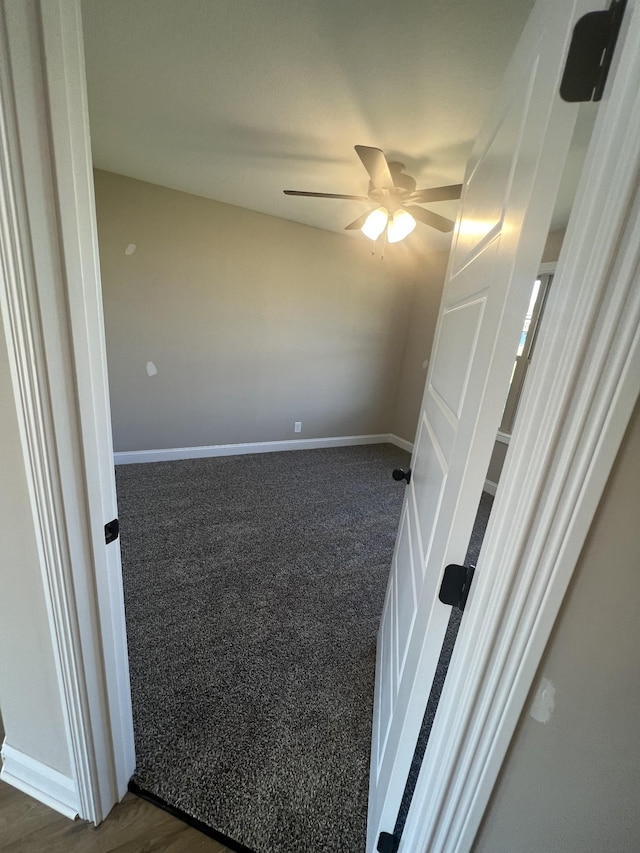 empty room featuring ceiling fan and dark colored carpet