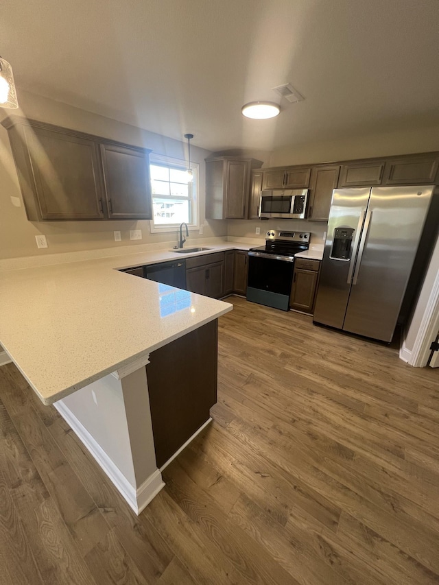 kitchen featuring pendant lighting, sink, stainless steel appliances, dark hardwood / wood-style flooring, and kitchen peninsula