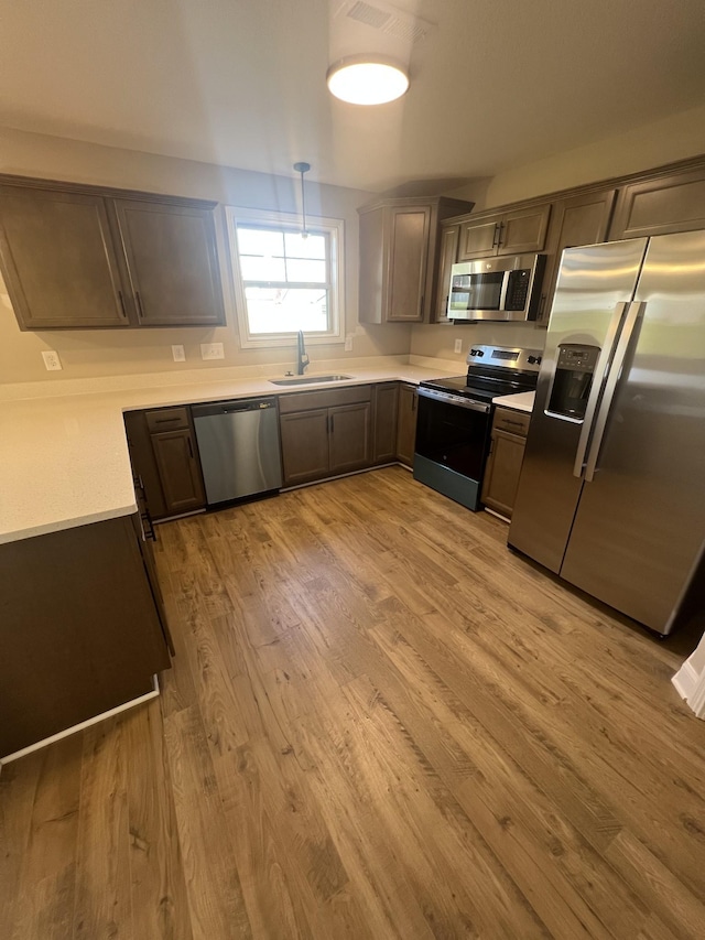 kitchen featuring sink, decorative light fixtures, light hardwood / wood-style floors, and appliances with stainless steel finishes