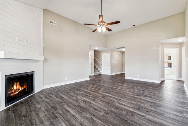 unfurnished living room with visible vents, a large fireplace, ceiling fan, stairs, and dark wood-style floors