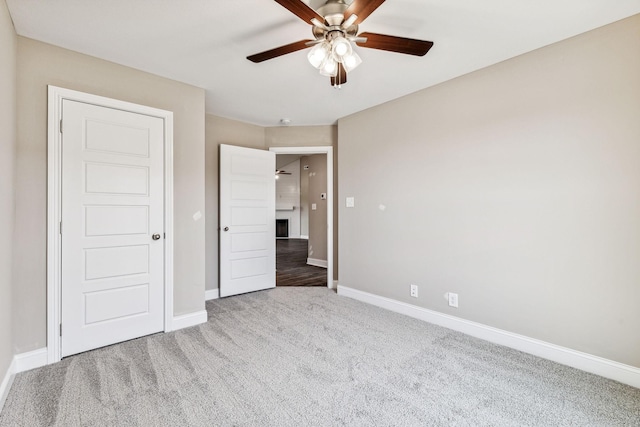 unfurnished bedroom with ceiling fan, a fireplace, baseboards, and carpet