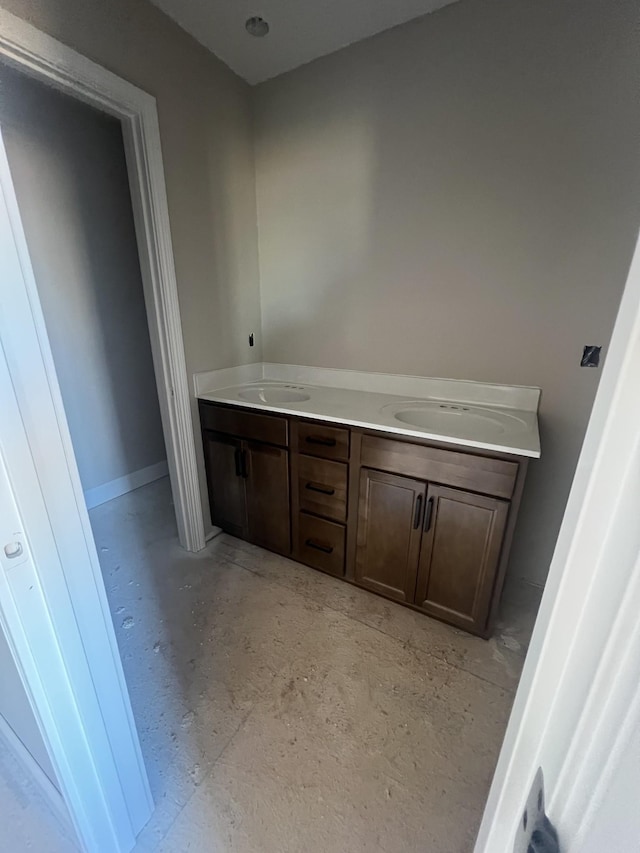 bathroom with double vanity, concrete flooring, baseboards, and a sink