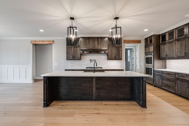 kitchen featuring dark brown cabinets, decorative light fixtures, a kitchen island with sink, and light hardwood / wood-style floors