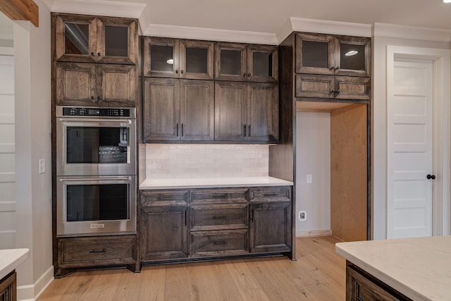 kitchen with dark brown cabinetry, crown molding, double oven, and light hardwood / wood-style flooring